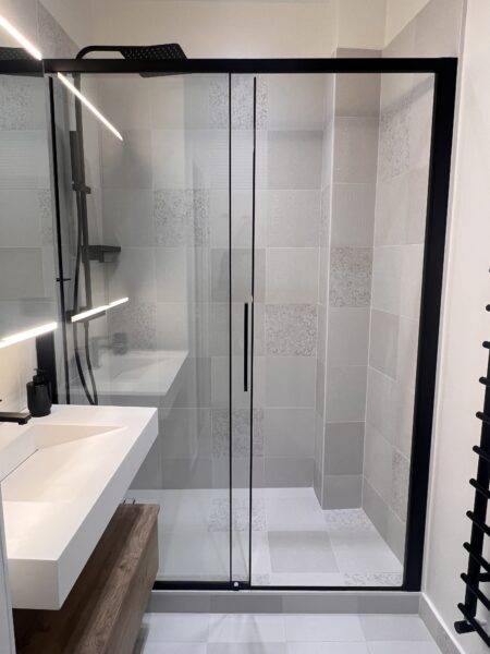 Vue d’une douche italienne avec paroi vitrée noire et carrelage gris texturé, dans une salle de douche rénovée à Saint-Mandé.