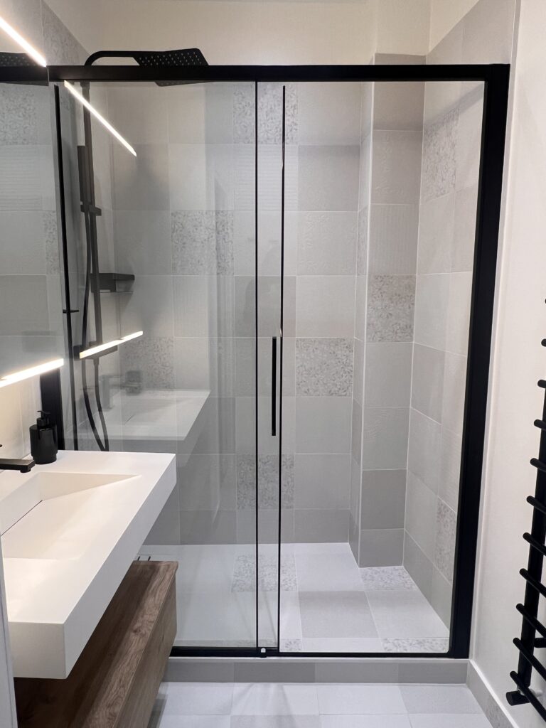 Vue d’une douche italienne avec paroi vitrée noire et carrelage gris texturé, dans une salle de douche rénovée à Saint-Mandé.