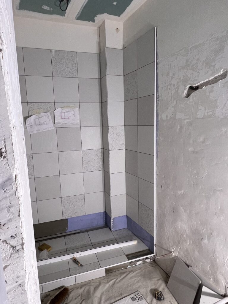 Vue de la pose du carrelage en cours dans une salle de douche en rénovation à Saint-Mandé, avec plans d’agencement affichés.