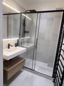 Vue complète d’une salle de douche rénovée à Saint-Mandé avec meuble vasque suspendu, paroi vitrée noire et carrelage texturé beige