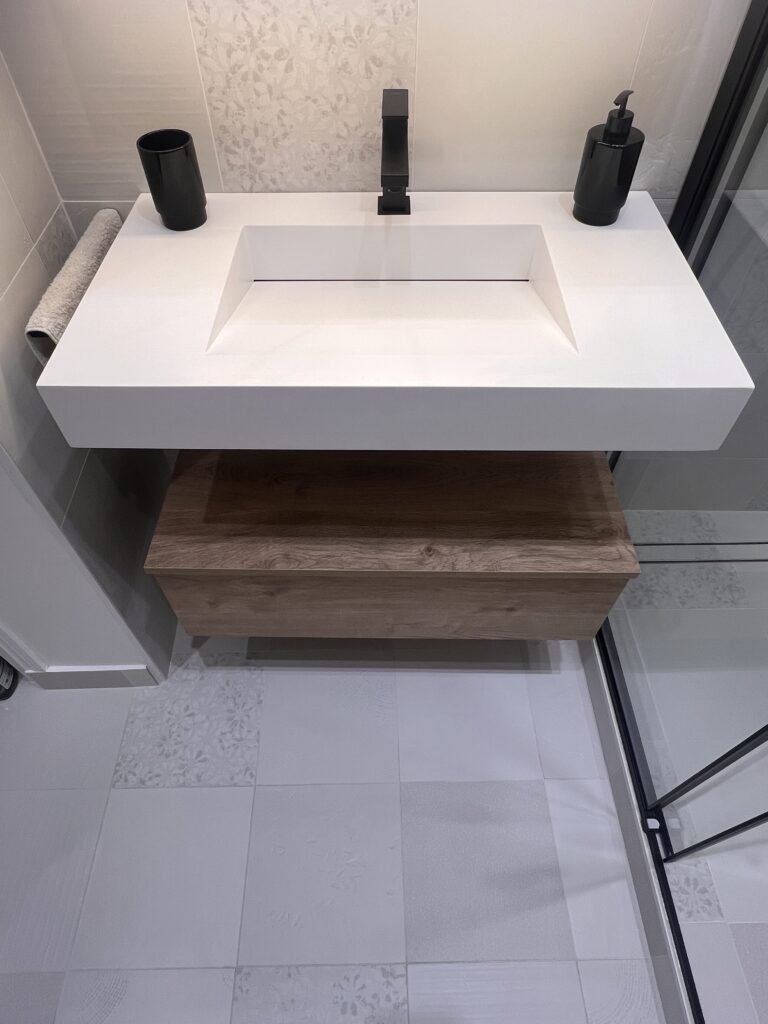 Gros plan sur un meuble vasque suspendu avec tiroir en bois, robinetterie noire et carrelage texturé, rénovation à Saint-Mandé.