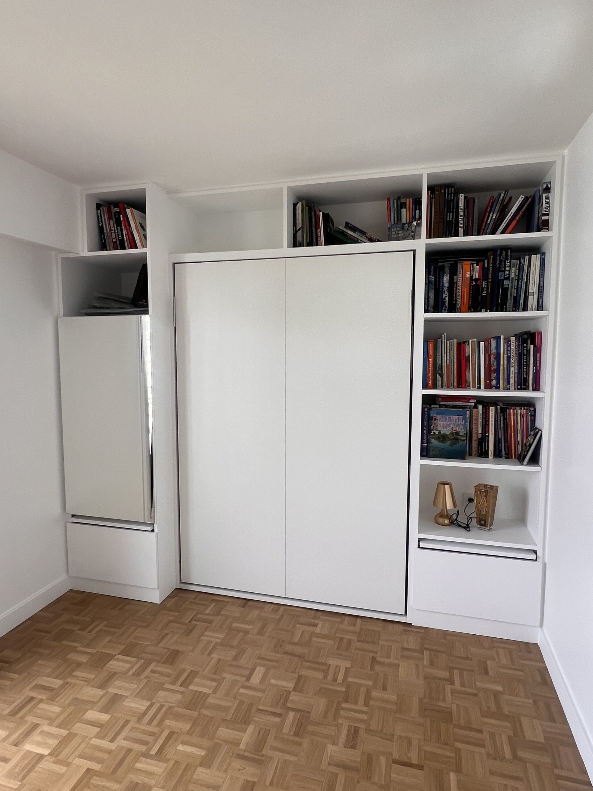 Bibliothèque blanche sur mesure intégrant un lit escamotable et des rangements fonctionnels