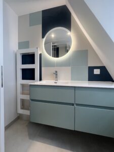 Salle de bains rénovée en architecture d’intérieur avec meuble vasque moderne vert pastel et miroir rond lumineux.