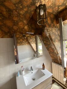 Lavabo et miroir de salle de bains avant rénovation par un architecte d’intérieur, style ancien avec revêtements muraux foncés.