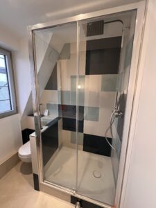 Salle de bains rénovée en architecture d’intérieur avec douche moderne, receveur extra-plat et parois vitrées, carrelage graphique bleu et gris.
