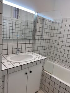 Salle de bains rénovée avec meuble vasque modernisé, miroir rétroéclairé et finitions noires décoratives.