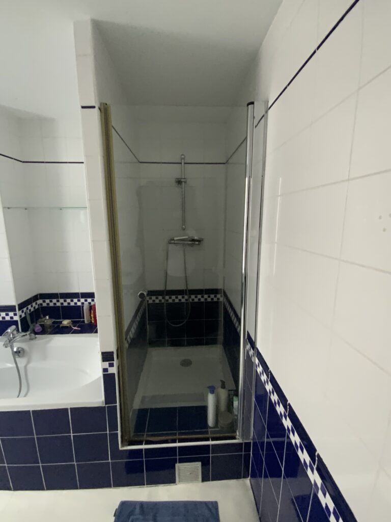 Douche ancienne à paroi vitrée avec faïence blanche et bleu foncé