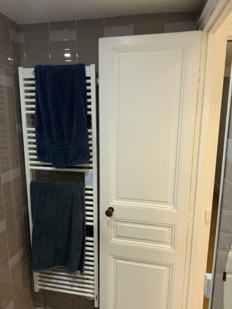 Radiateur mural et porte dans une salle de douche avant rénovation à Paris 9.