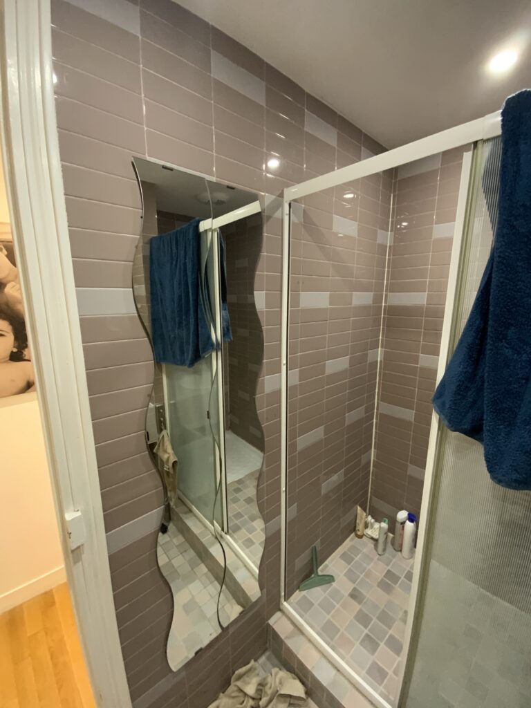 Miroir mural ondulé et cabine de douche en aluminium blanc avant rénovation à Paris 9.