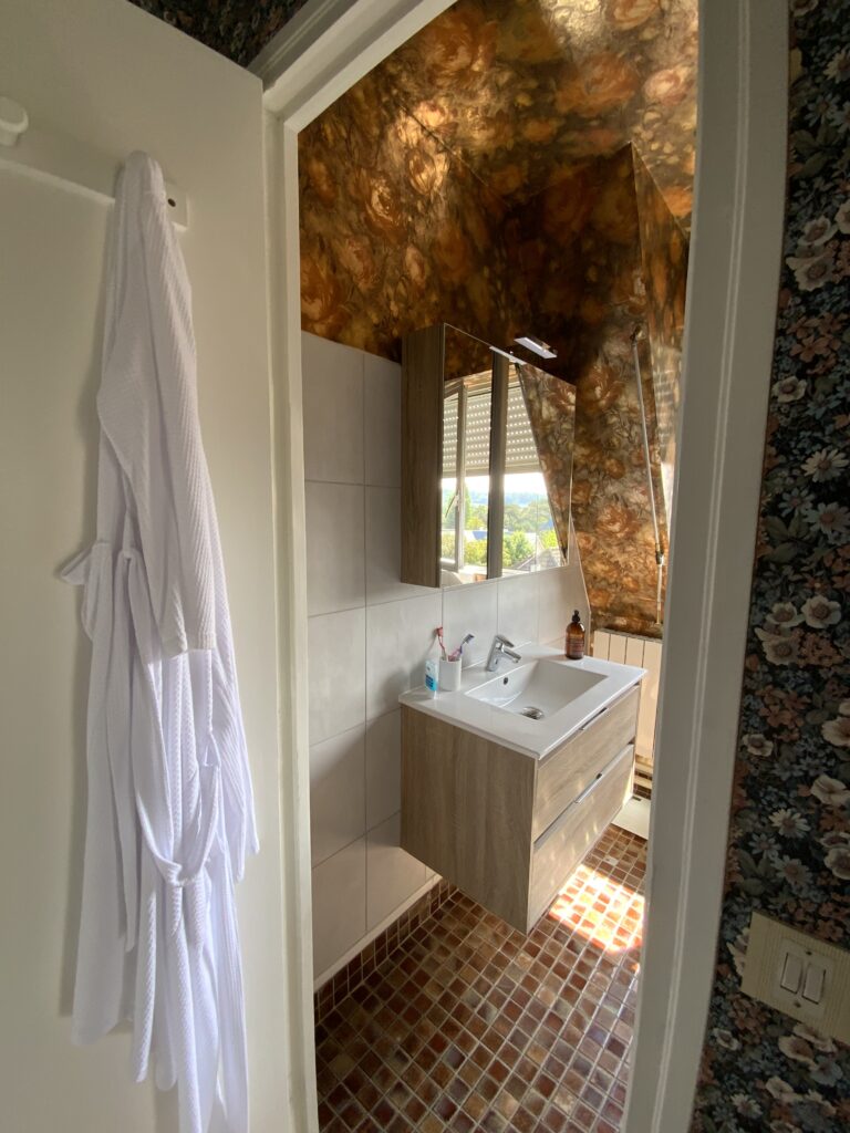 Vue d’ensemble de la salle de bains sous combles avant rénovation avec meuble vasque et sol en petits carreaux