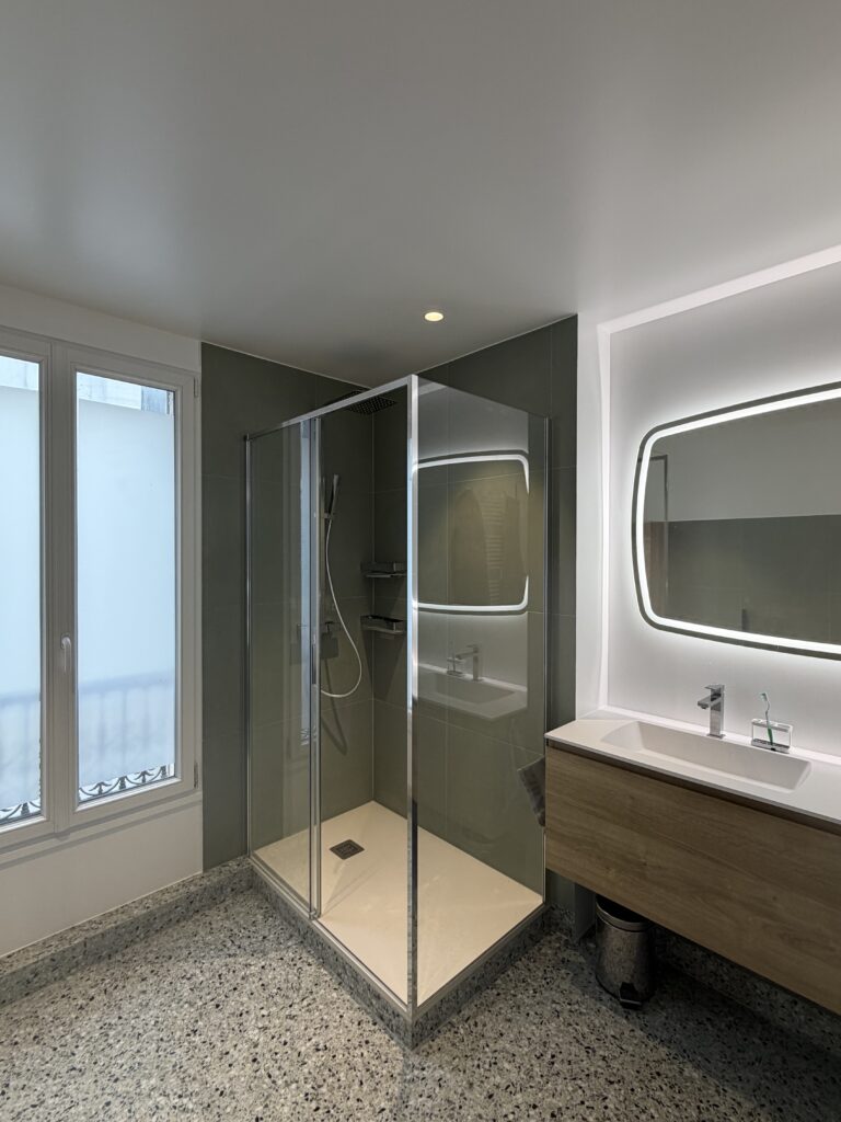 Salle de bains rénovée à Paris 9 avec douche vitrée, carrelage vert sauge et meuble vasque suspendu