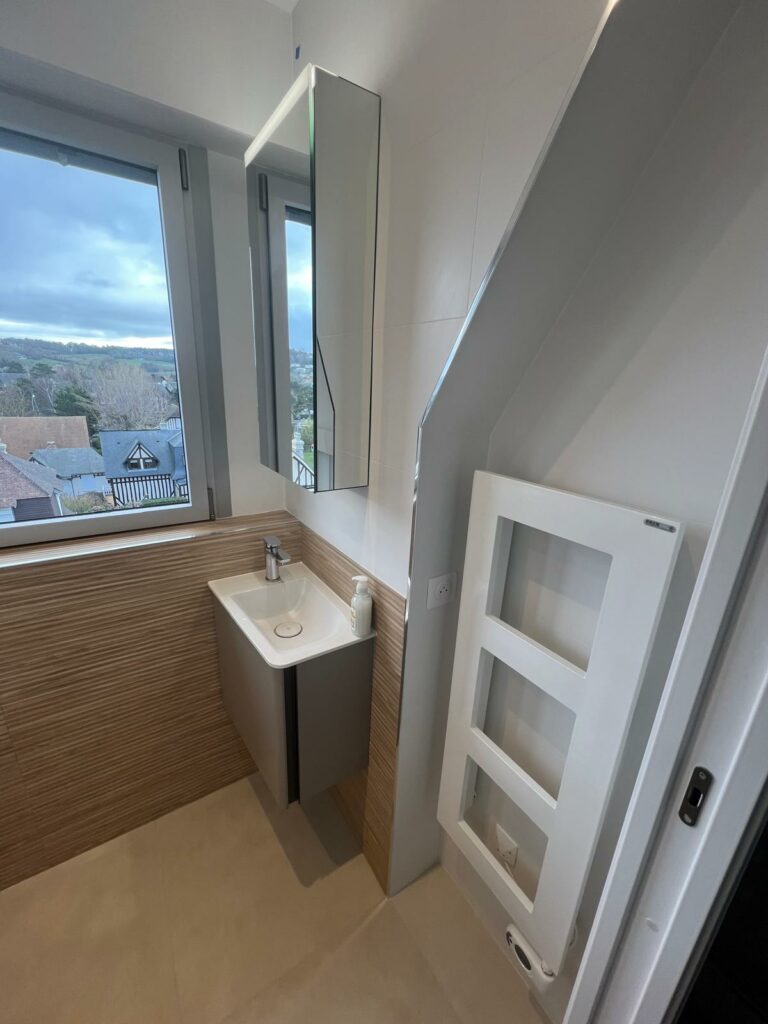 Petite salle de bains sous combles rénovée à deauville avec meuble vasque, miroir et radiateur blanc mural