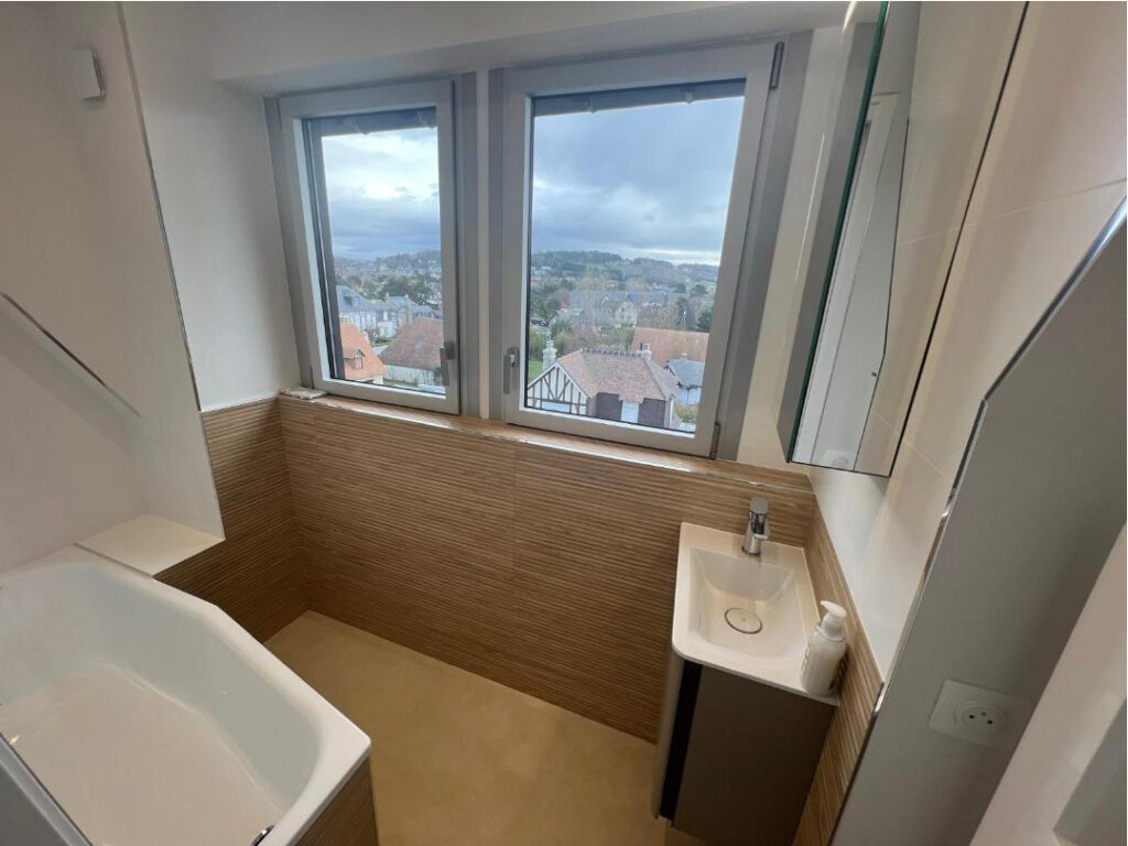 Vue d’ensemble d’une petite salle de bains sous combles rénovée avec baignoire, vasque et carrelage clair à Deauville