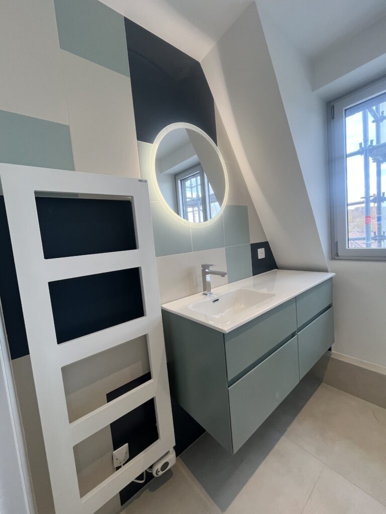 Meuble vasque suspendu et miroir rond lumineux dans une salle de douche sous combles rénovée