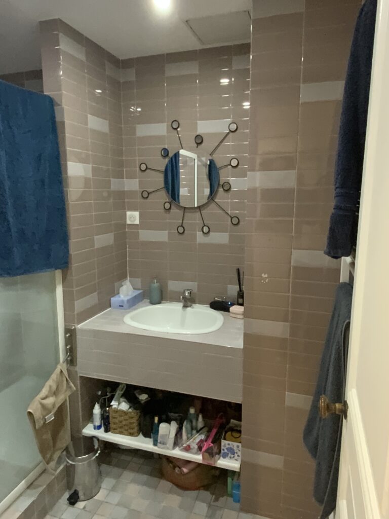 Meuble vasque carrelé avec rangements visibles et miroir soleil, avant rénovation à Paris 9.